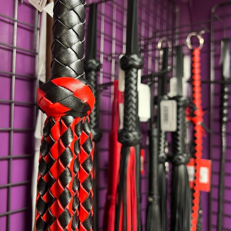 accessoires bdsm fetish Nimes Fouets en cuir rouge et noir accrochés à un mur violet.